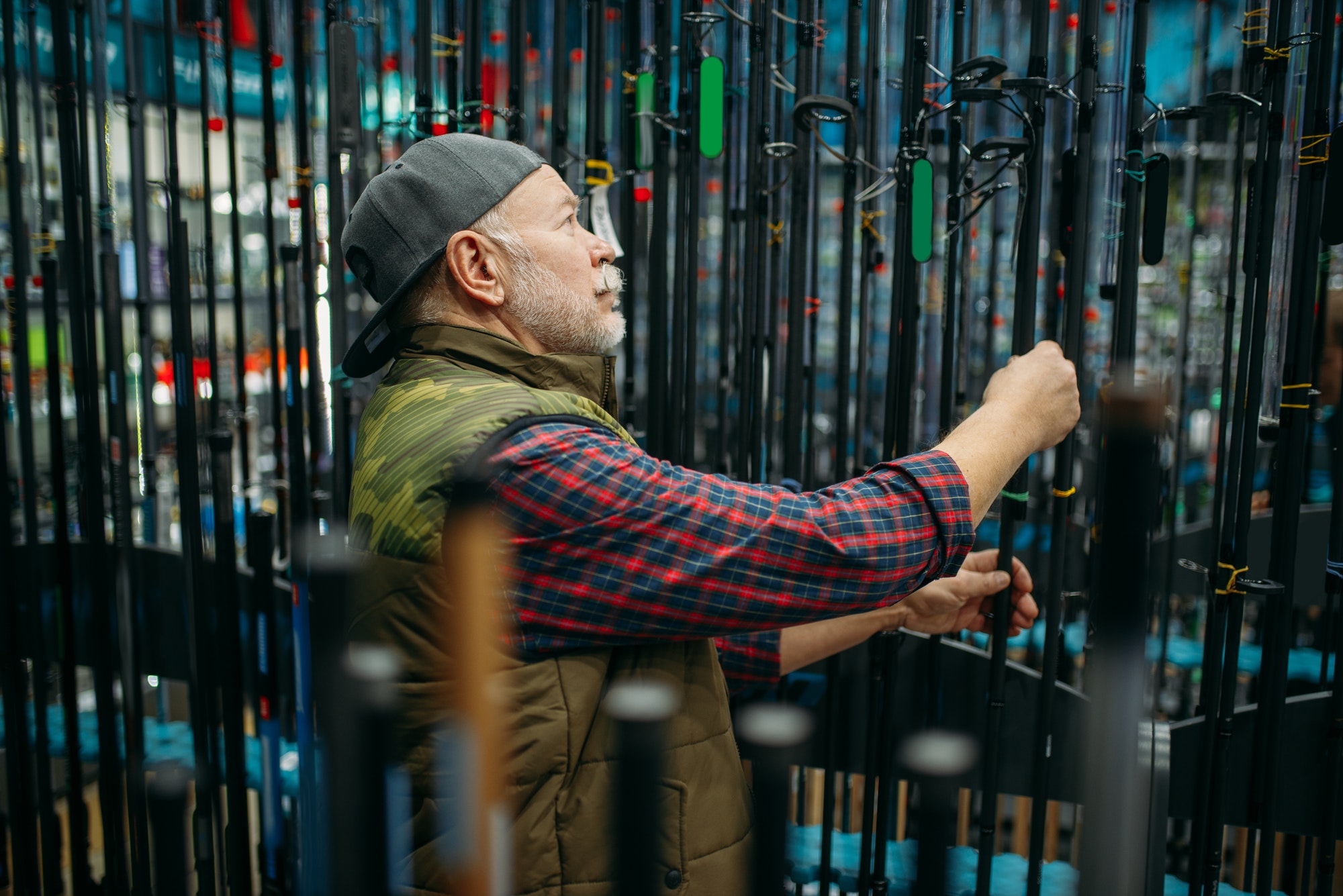 Male angler choosing rod in fishing shop