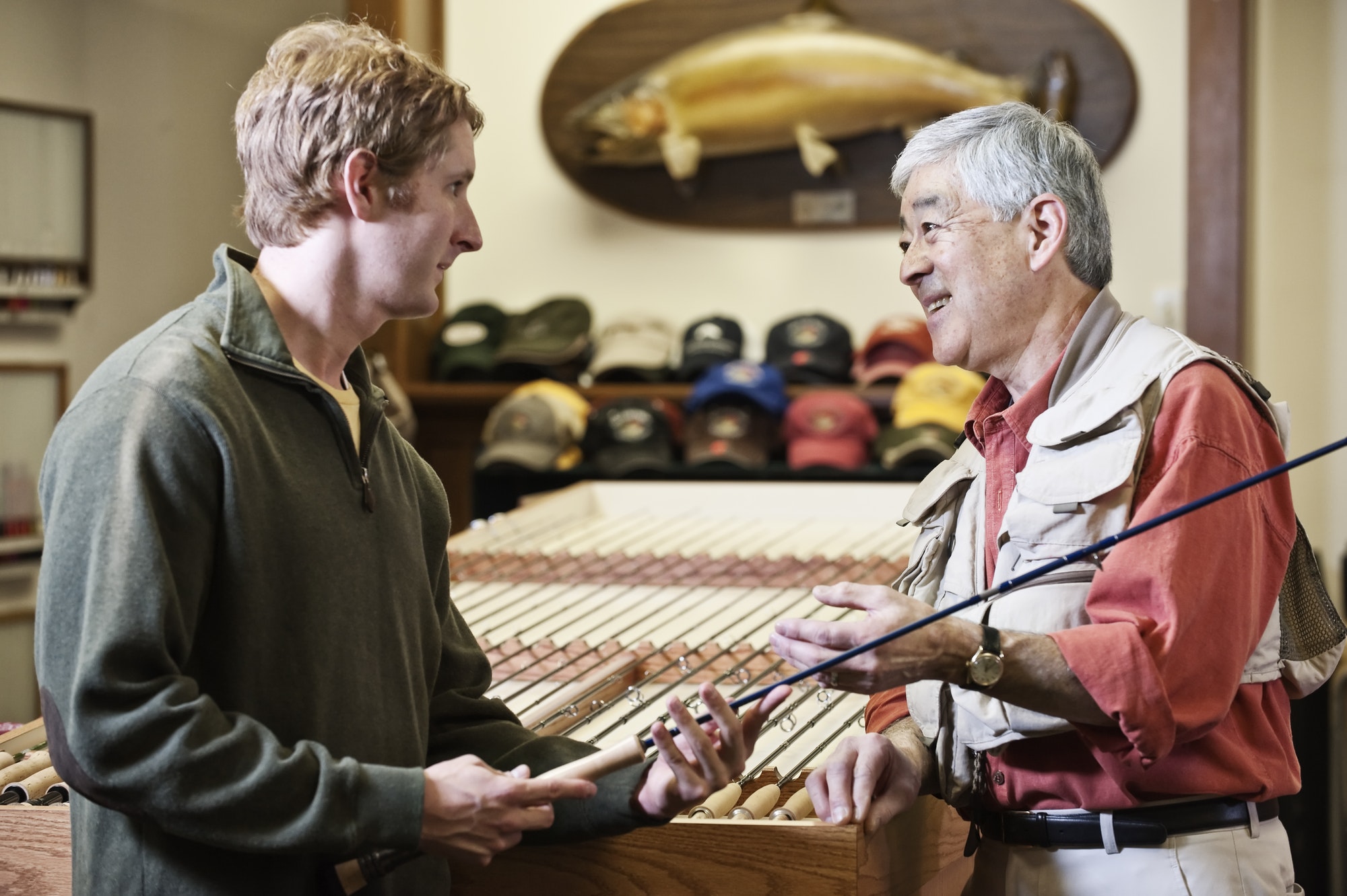 Male owner of a retail fly-fishing shop talking to a young caucasian customer sharing expertise